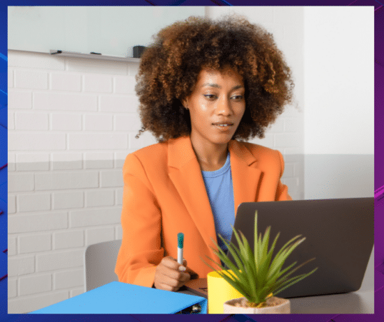 a woman sitting at a desk with a laptop and a pen; Imposter-Syndrome-Trap-Black-Women-Feel-Isolated-in-Leadership
