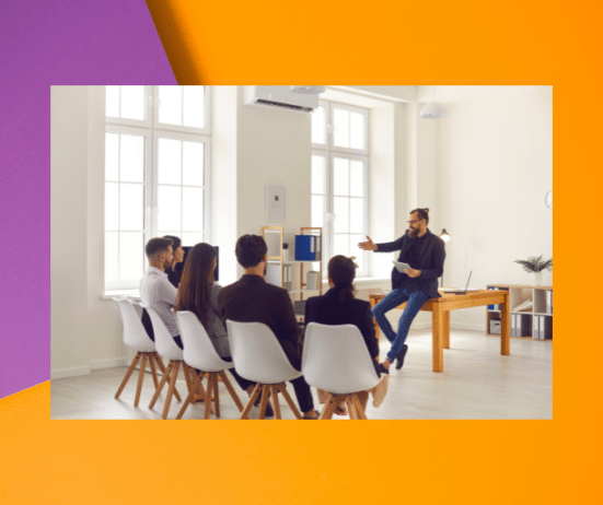 a man sitting on a table with a group of people in a room; signs-of-a-sabotaging-bos; Twanna Carter best Black coach for women